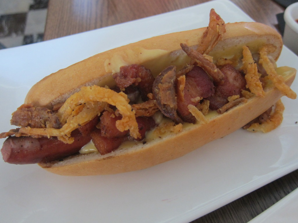 The Manly Dog with beer-cheddar cheese, minced bacon, onion strings, house ketchup and mustard spread